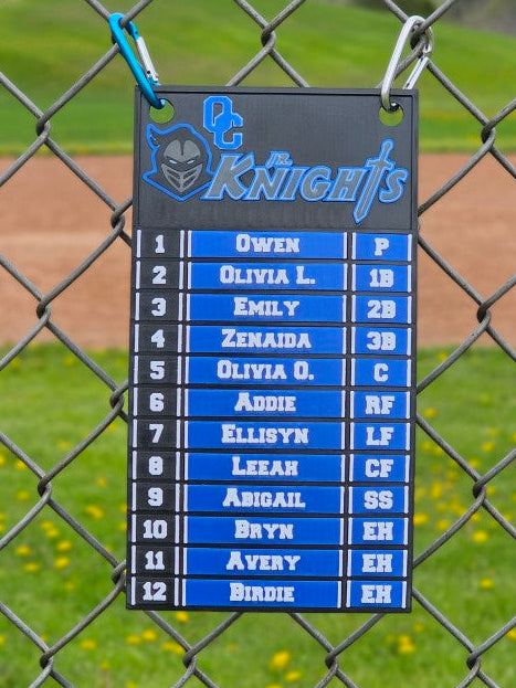 Blue and black sports team roster tag on a chain-link fence with a baseball field background